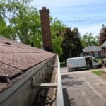 A brown shingle roof with a truck parked in front, set against a clear blue sky