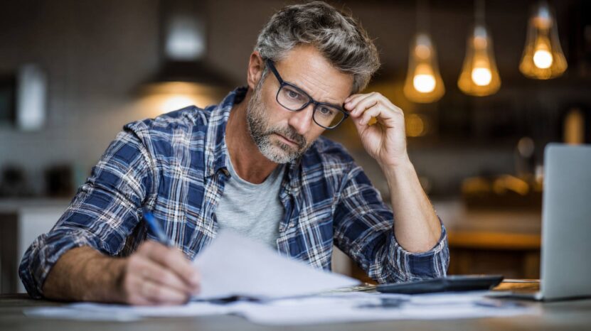 Man reviewing bills and paperwork at a table with a calculator and laptop