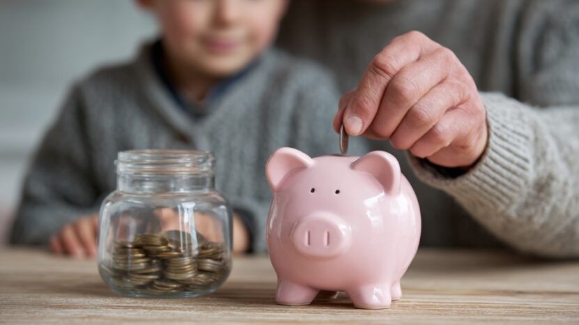 Adult placing a coin into a piggy bank while a child sits nearby