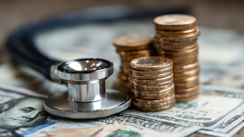Stethoscope and stacks of coins placed on dollar bills representing medical costs