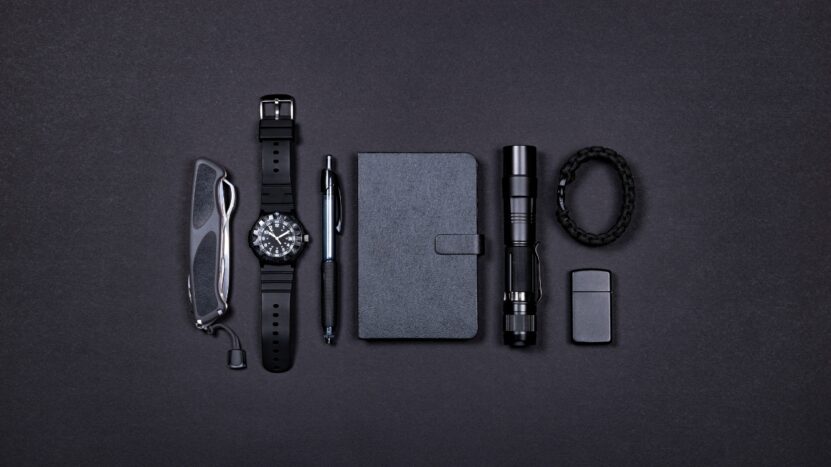 Everyday carry items are lined up on a dark surface