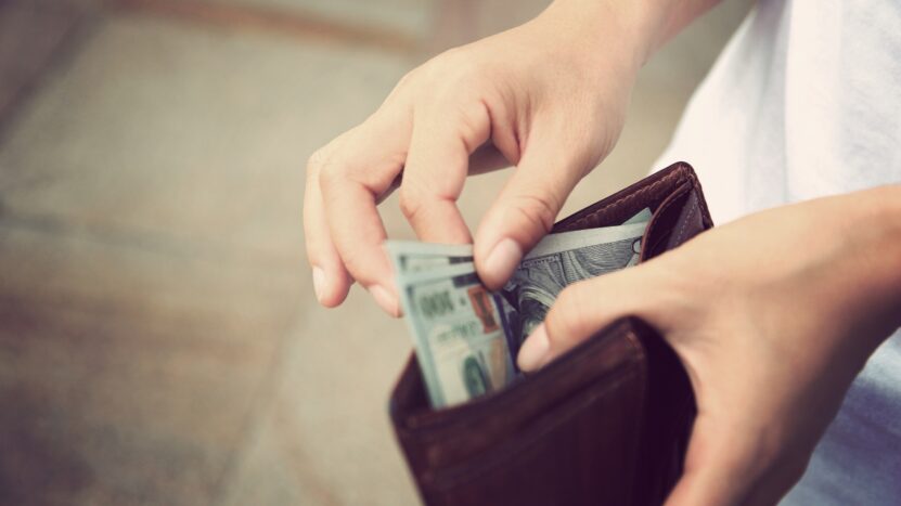 A person takes cash out of a brown leather wallet