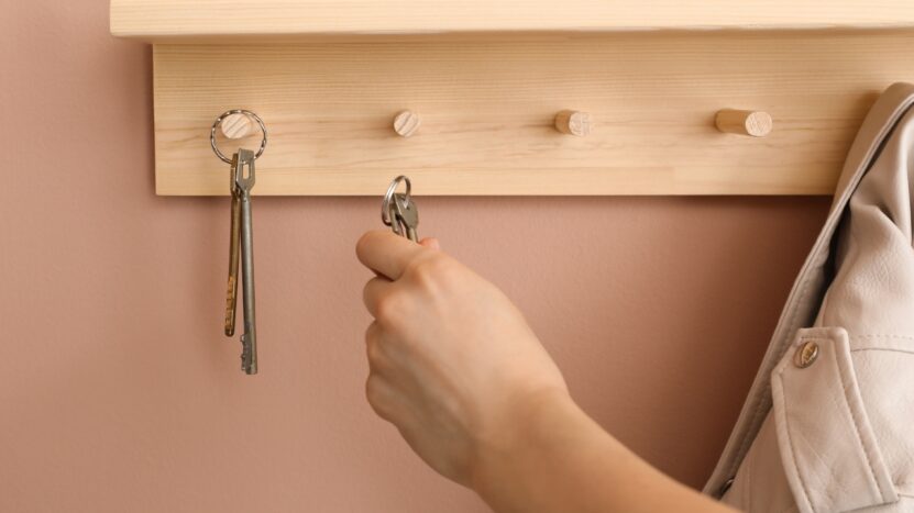 A person hangs keys on a wooden wall rack near the door