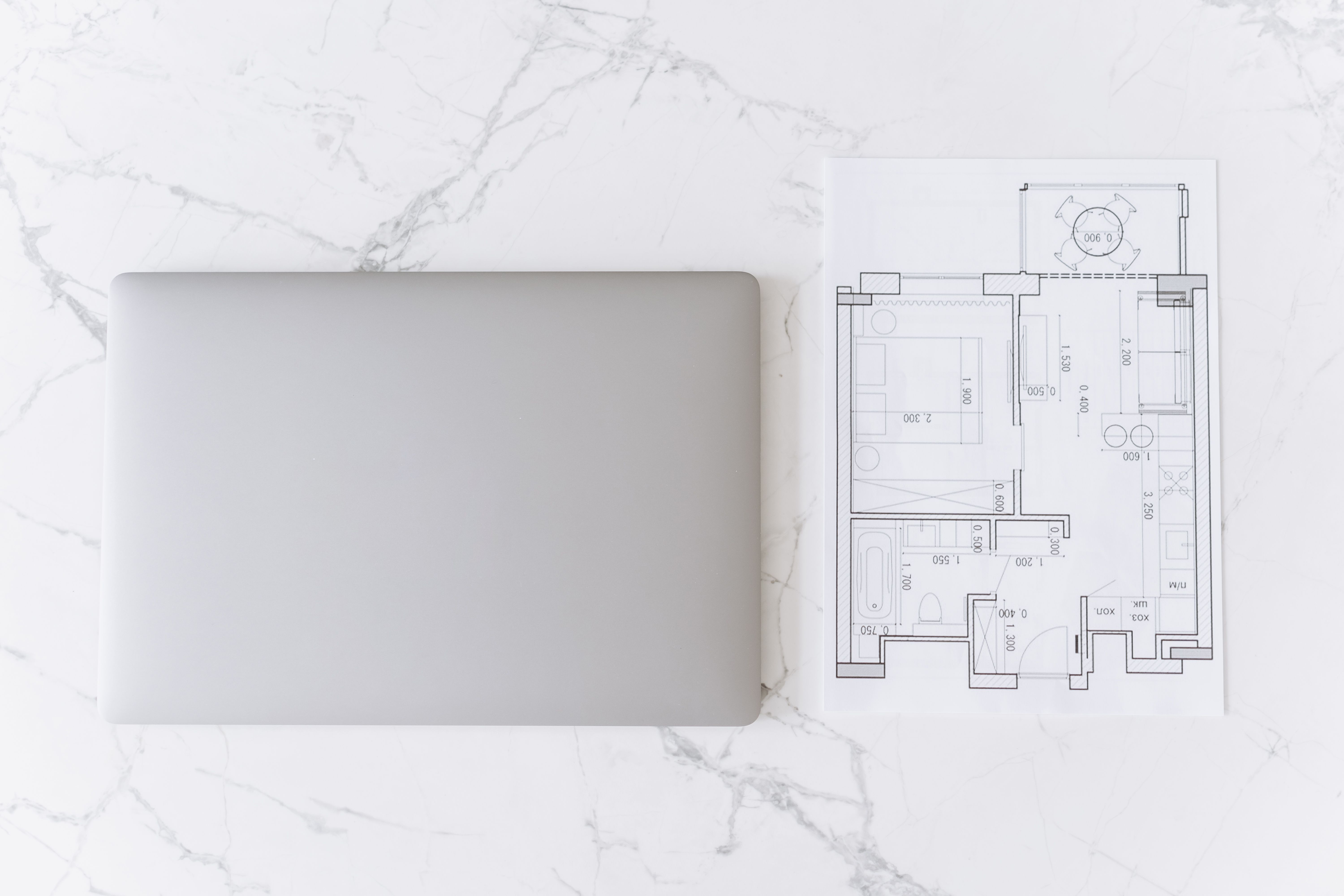 Laptop and architectural blueprint arranged on a desk for digital home renovation planning.