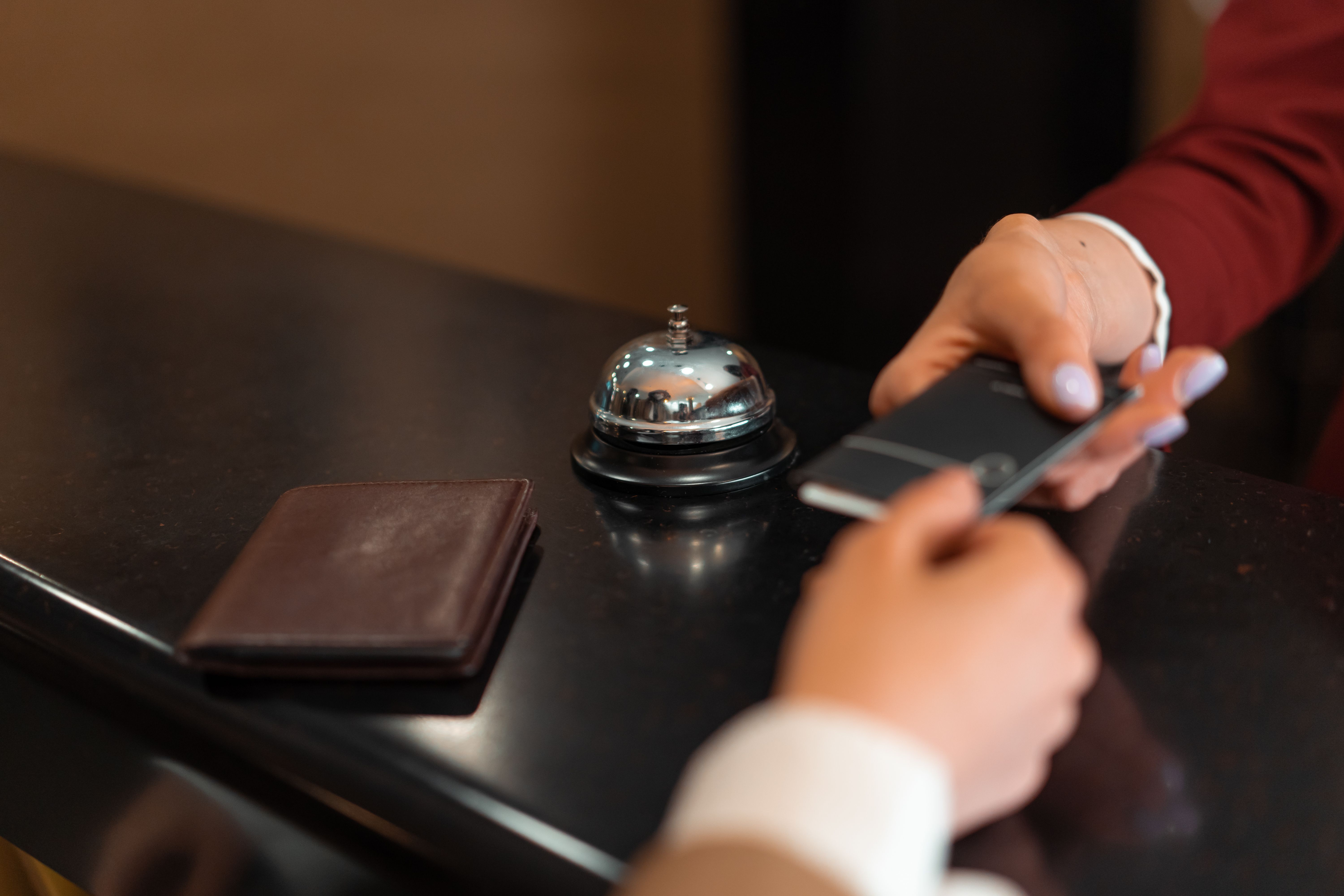 Guest checking in at a hotel reception using a smartphone and payment card.